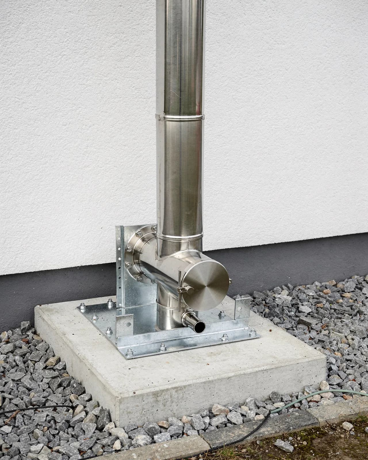 Fuß der Anlage auf einer verzinkten Standkonsole auf einem Betonsockel, mit T-Stück, runder Reinigungstür und Kondensatablauf.