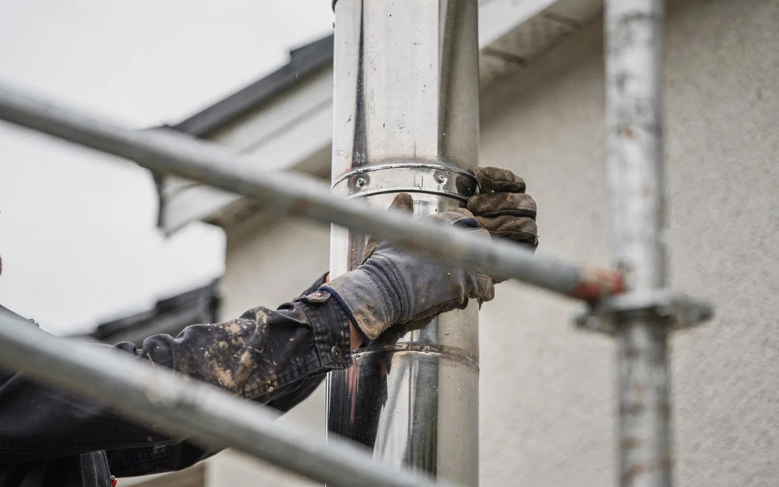 Behandschuhte Hände setzen einen Rohrschuss auf die bereits stehende Anlage, aufgenommen von Gerüsthöhe.