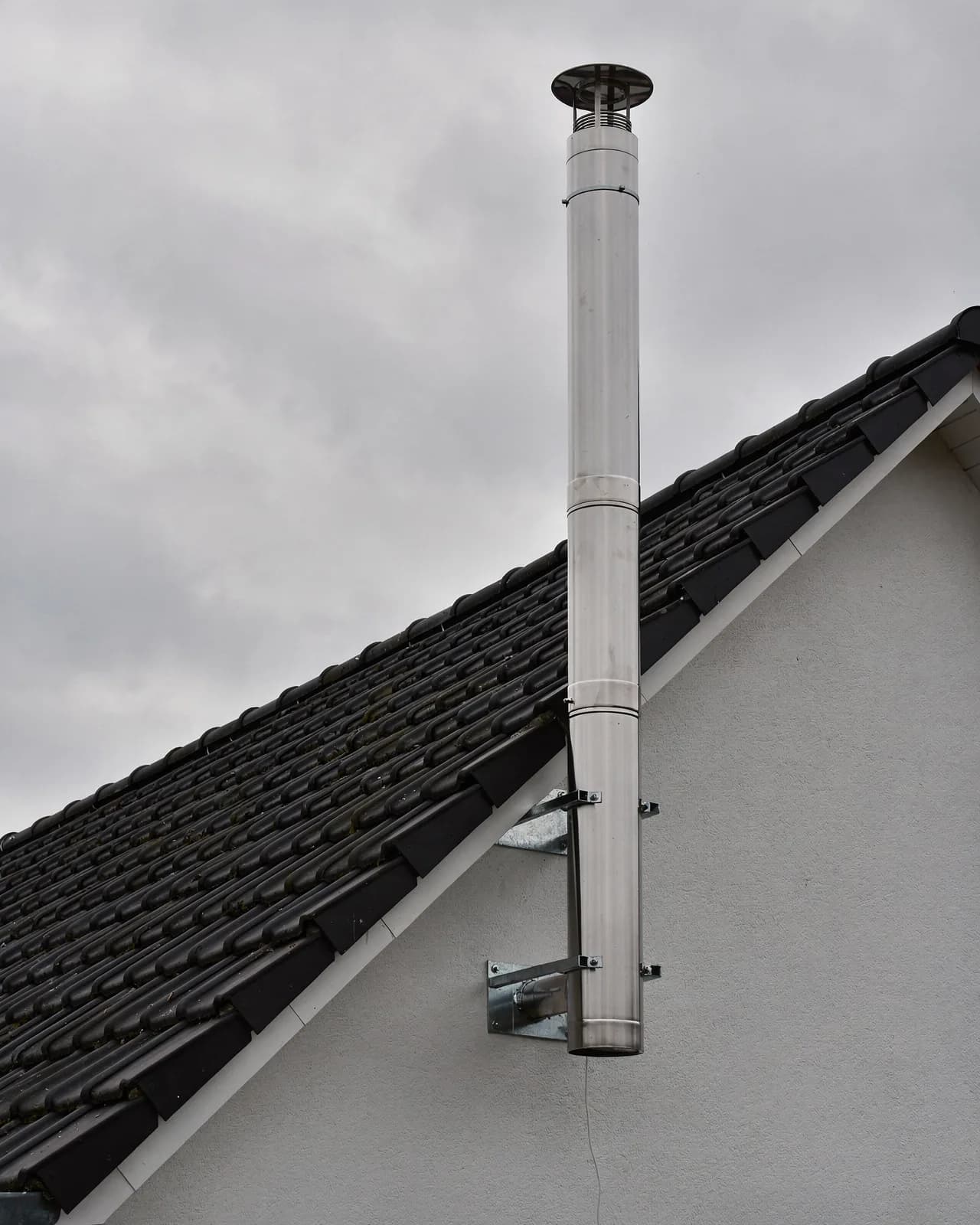 Das Rohr läuft an der Giebelwand am Dachrand vorbei und endet mit einer Haube frei über dem First.
